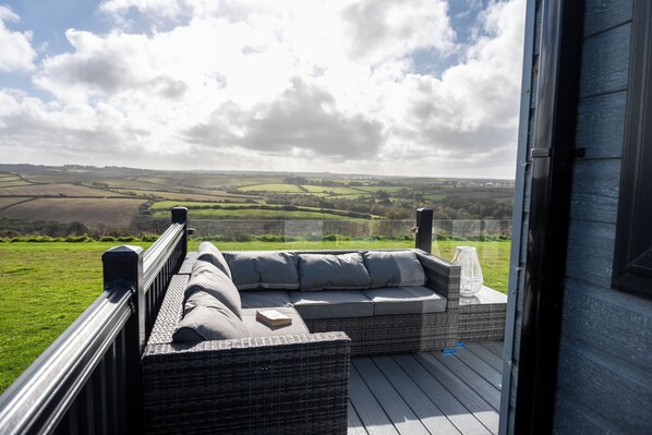 A wicker sofa with cushions on an outdoor deck with a view of rolling hills.
