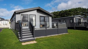 Une maison mobile moderne, avec une façade grise, de grandes fenêtres et un petit porche doté de marches menant à l’entrée.