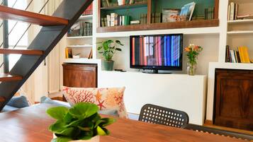 A modern living room with a wooden staircase, a television, and a bookshelf filled with books and decorative items.