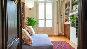 A bedroom with a bed, a radiator, a bookshelf, and a potted plant.