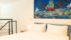 A hotel room with a bed, a nightstand, a painting on the wall, and a staircase.