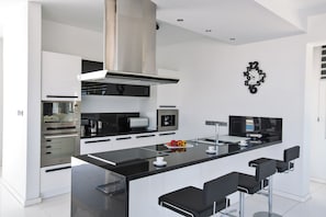 Een moderne keuken met een centraal eiland, barstoelen, roestvrijstalen apparatuur en een klok aan de muur.