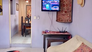 A room with a television, a sofa, a dining table, and a mirror.