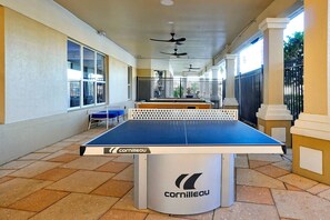 A table tennis table with a white and blue surface, branded with 'Cornilleau'. The setting includes tiled flooring and a covered area with columns and ceiling fans. - Mickey s Welcome Inn - Closest Resort to Disney (Kissimmee)
