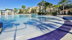 A swimming pool with a tiled edge, surrounded by palm trees and a building with balconies. - Mickey s Welcome Inn - Closest Resort to Disney (Kissimmee)