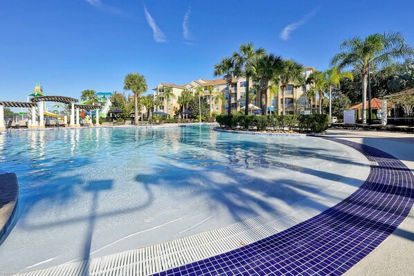 A swimming pool with a tiled edge, surrounded by palm trees and a building with balconies. - Mickey s Welcome Inn - Closest Resort to Disney (Kissimmee)