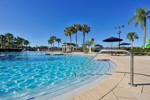 Une piscine d’un bleu éclatant, bordée d’une terrasse carrelée et entourée de palmiers et de parasols.