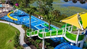 A water park with a blue pool, green slides, and a yellow canopy. - Mickey s Splash Pad 2 Miles to Disney (Kissimmee)