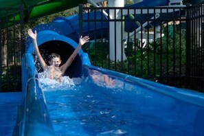 A water slide with a child at the top, surrounded by a metal fence and greenery. - Mickey s Splash Pad 2 Miles to Disney (Kissimmee)