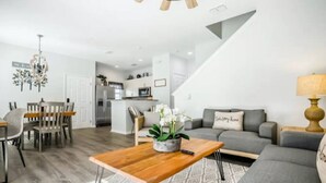A modern living room with a grey sofa, a wooden coffee table, and a dining area with a wooden table and chairs. - Fantastic Designer 4 BD TH 12 Mins to Disney (Kissimmee)