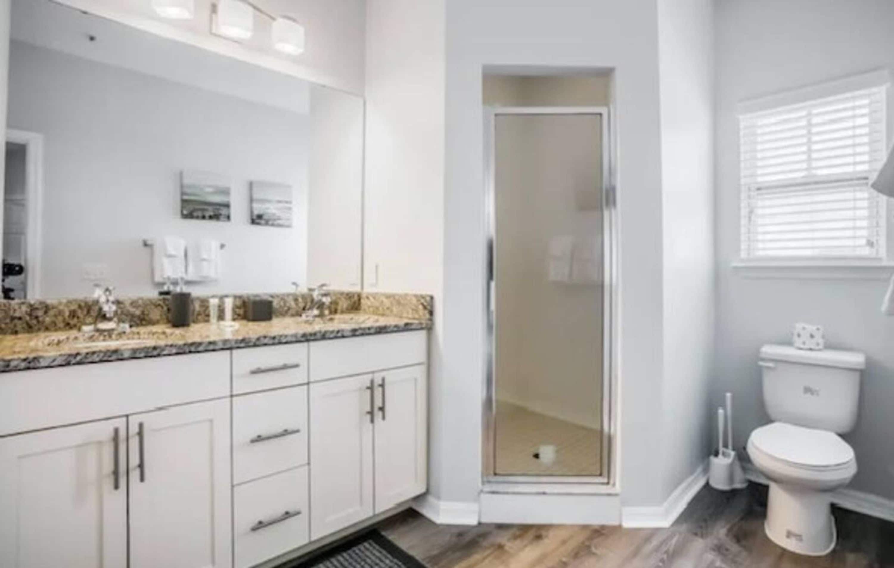 A modern bathroom with a shower enclosure, a toilet, and a vanity with a granite countertop.