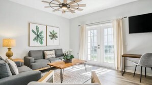 A modern living room with a grey sofa, a wooden coffee table, and a ceiling fan. - Fantastic Designer 4 BD TH 12 Mins to Disney (Kissimmee)
