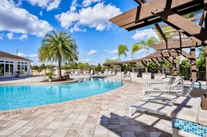 A swimming pool with lounge chairs, palm trees, and a covered area with wooden beams. - Fantastic Designer 4 BD TH 12 Mins to Disney (Kissimmee)