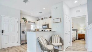 A modern kitchen with white cabinets, a built-in microwave, and a refrigerator. There are two striped chairs and a small island with a sink. - Fantastic Designer 4 BD TH 12 Mins to Disney (Kissimmee)