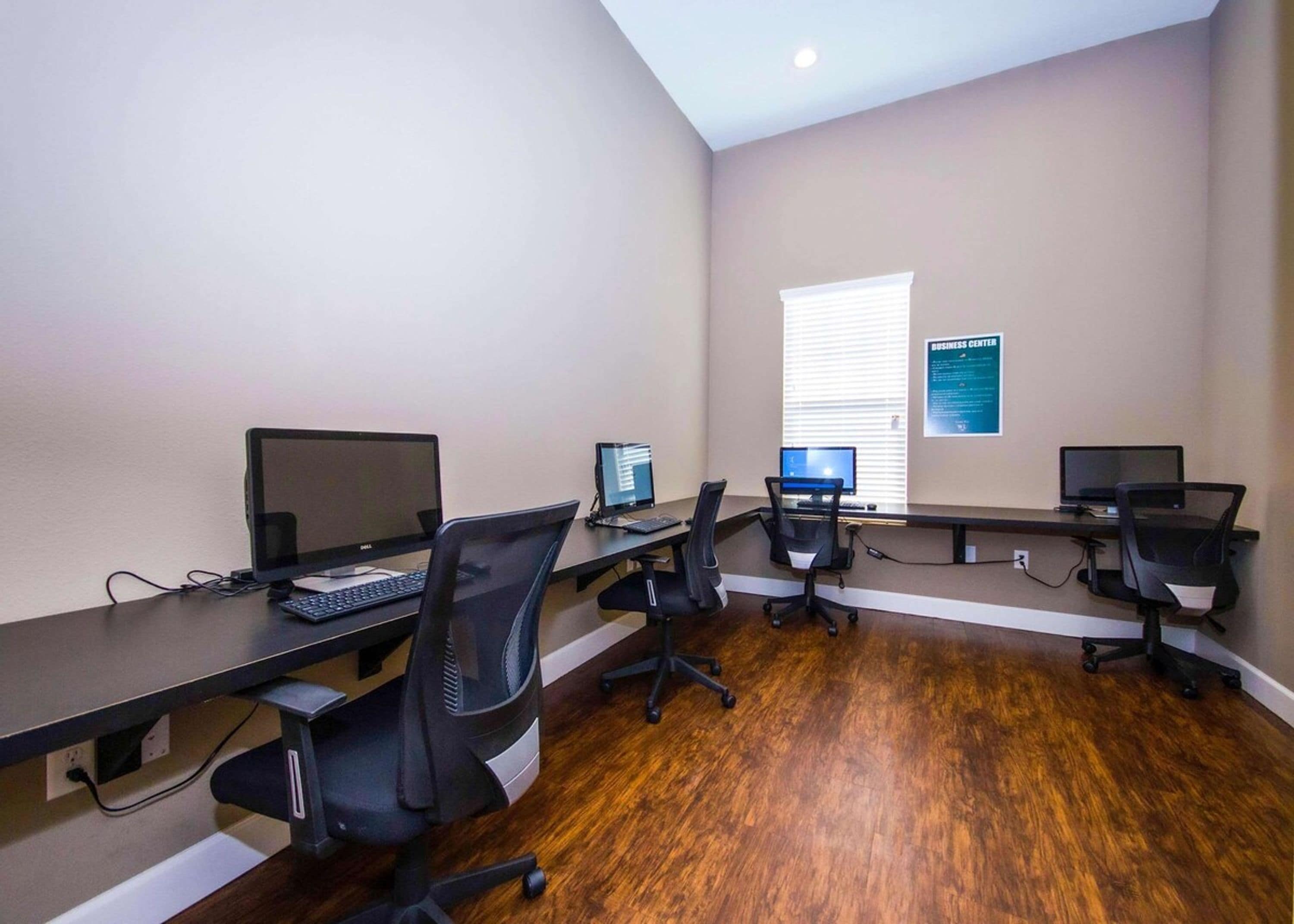 A business center with multiple computer stations, black office chairs, and a bulletin board on the wall.