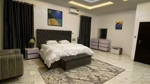 A modern bedroom with a large bed, a sofa, a TV, and a ceiling light. - Lekki Grand Apartment (Lekki)