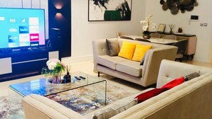 A modern living room with a sofa, coffee table, and a flat-screen TV. - Lekki Grand Apartment (Lekki)