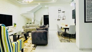 A modern living room with a sofa, a striped armchair, a coffee table, and a dining area with a table and chairs. - Lekki Grand Apartment (Lekki)