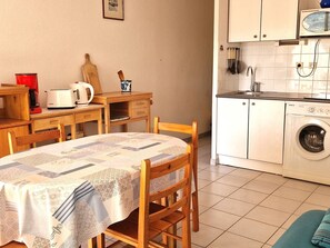 Cocina compacta con lavadora, cafetera y una mesa de madera con sillas.