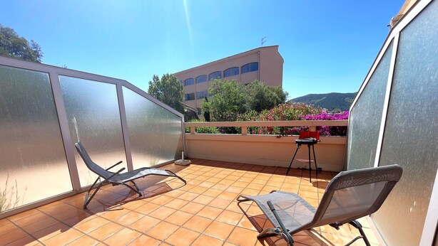 A balcony with tiled flooring, two metal chairs, a small table, and a building in the background. - Charming T2 with terrace between beaches in Banyuls-sur-Mer (Banyuls-sur-Mer)