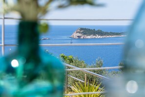 A coastal view with a small island, a sailboat, and a railing in the foreground.