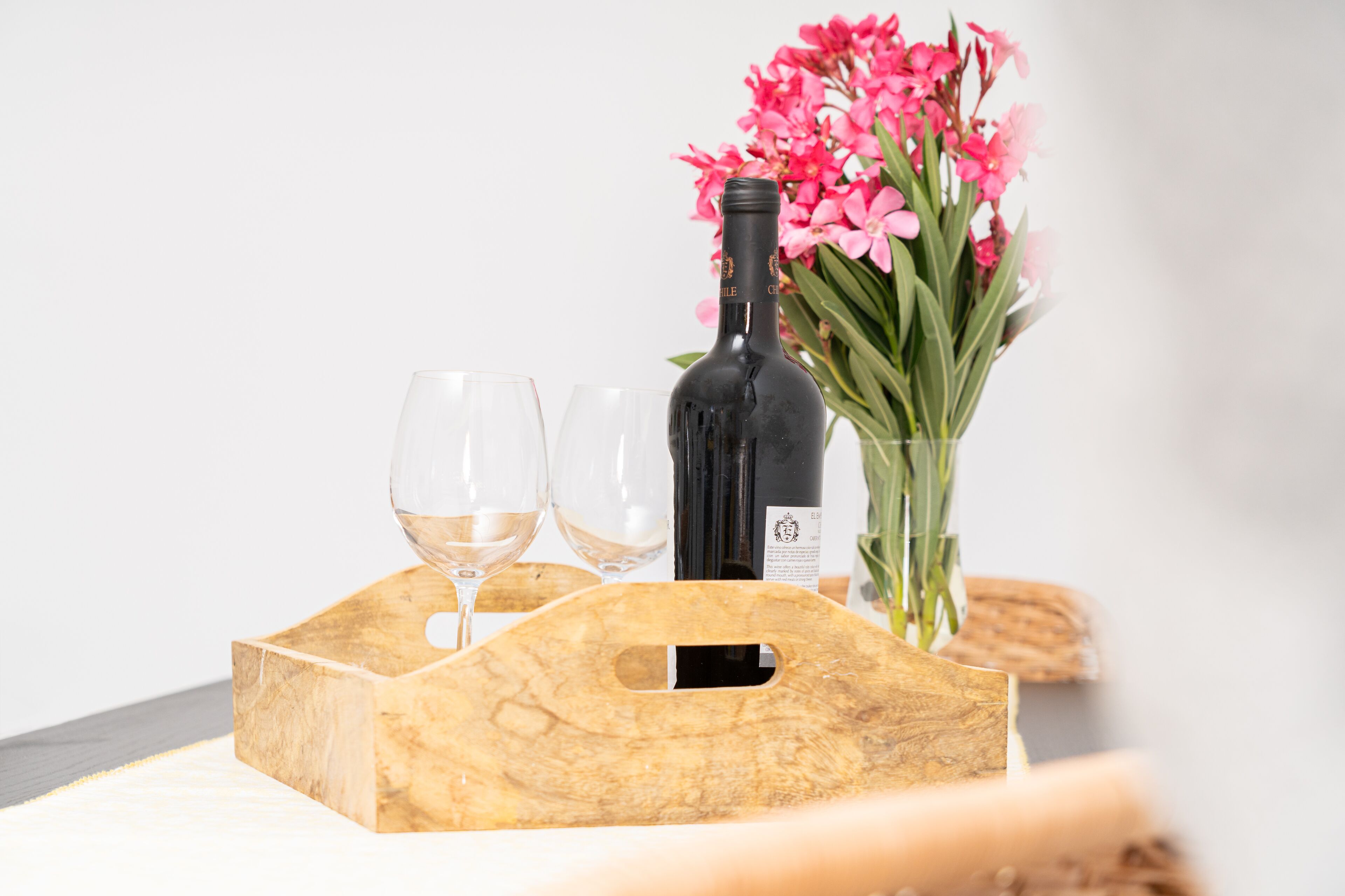 Ein Holztablett mit einer Weinflasche und zwei Gläsern, dazu ein Strauß rosa Blumen.