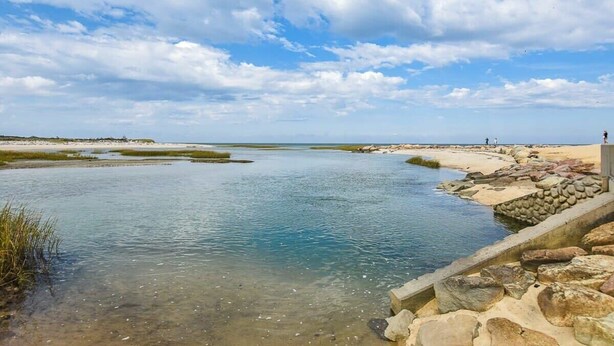 Un paysage côtier avec une rivière paisible, une rive rocheuse et un ciel dégagé.