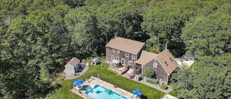 A house surrounded by dense forest, with a swimming pool and a small shed.
