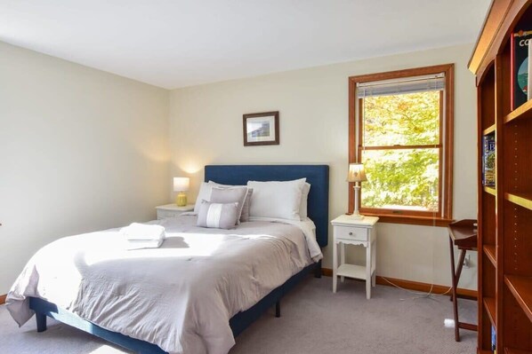 Une chambre à coucher avec un lit, des tables de chevet, une fenêtre et une bibliothèque.