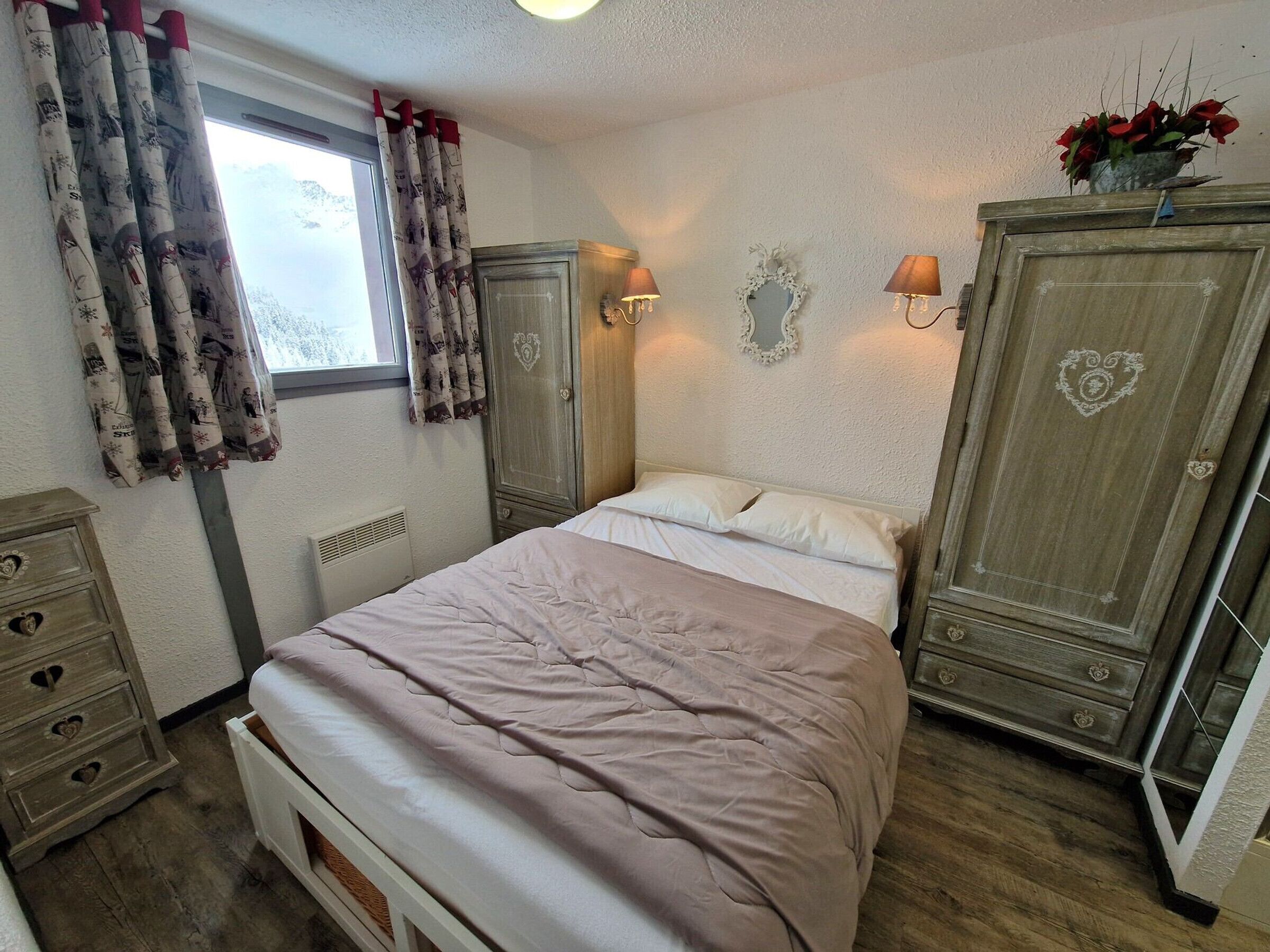 A bedroom with a bed, two wardrobes, a dresser, and a window with curtains.