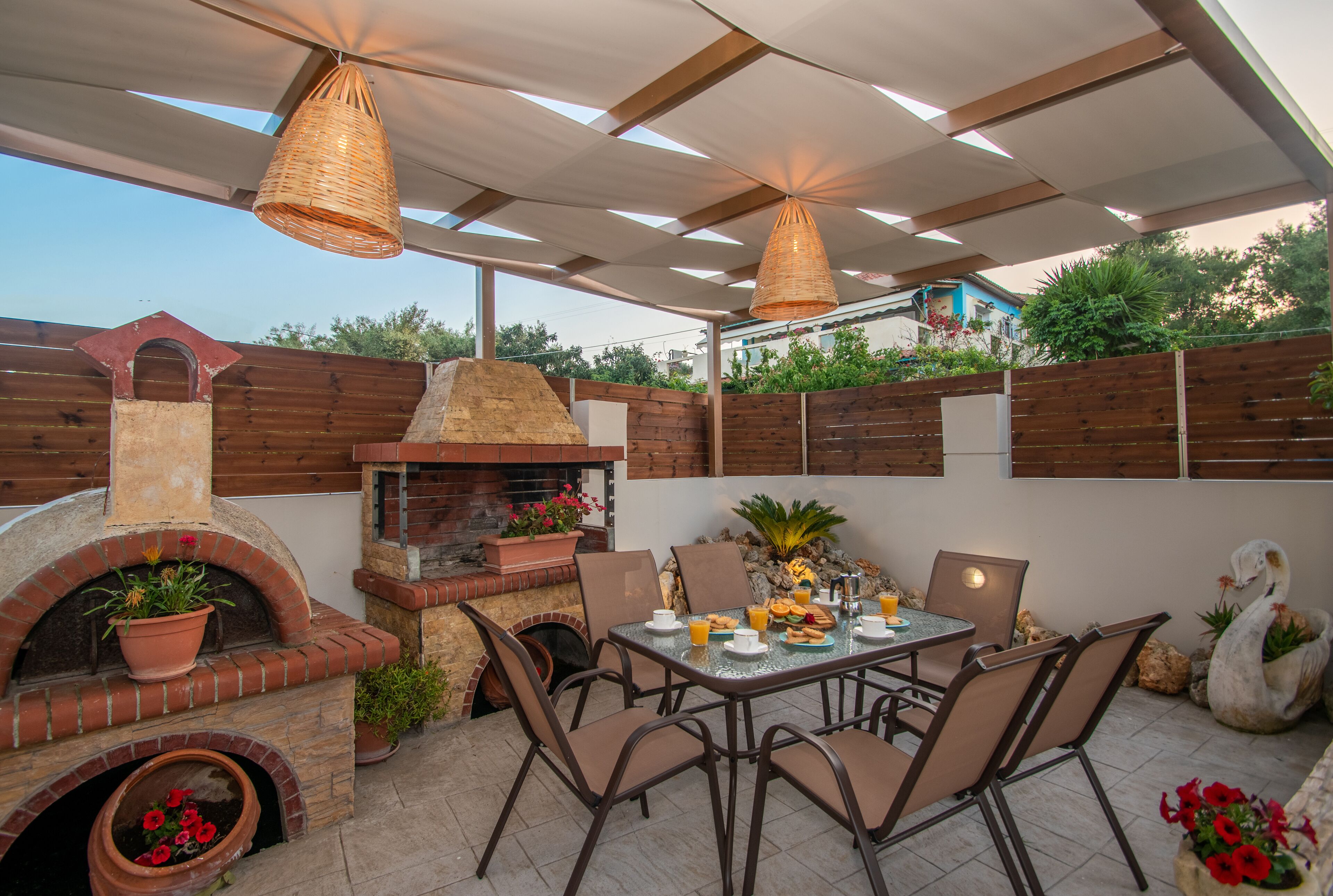 Een terras buiten met een bakoven, een eettafel, stoelen en potplanten.