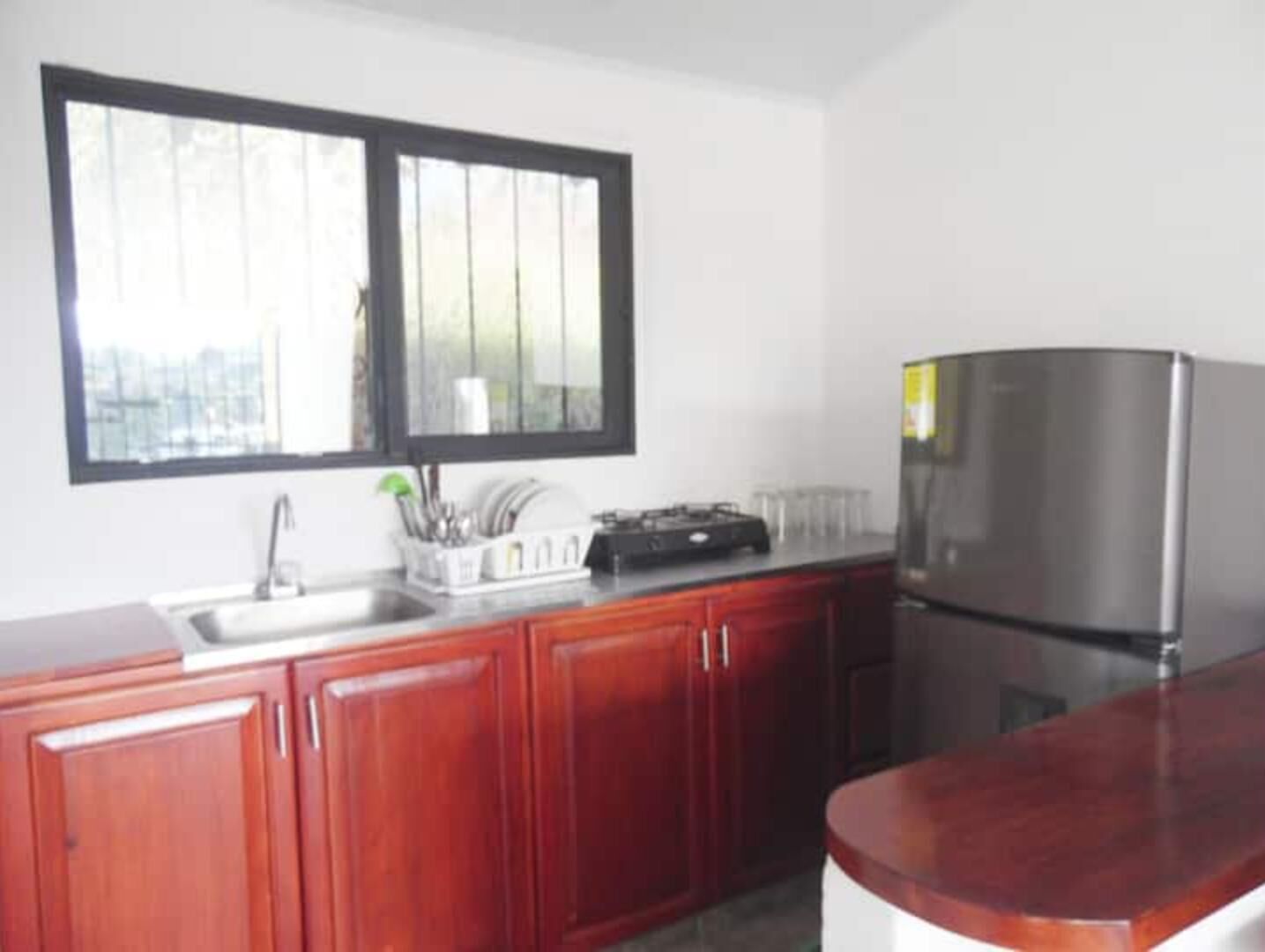 A kitchen with wooden cabinets, a stainless steel refrigerator, and a window above the sink.