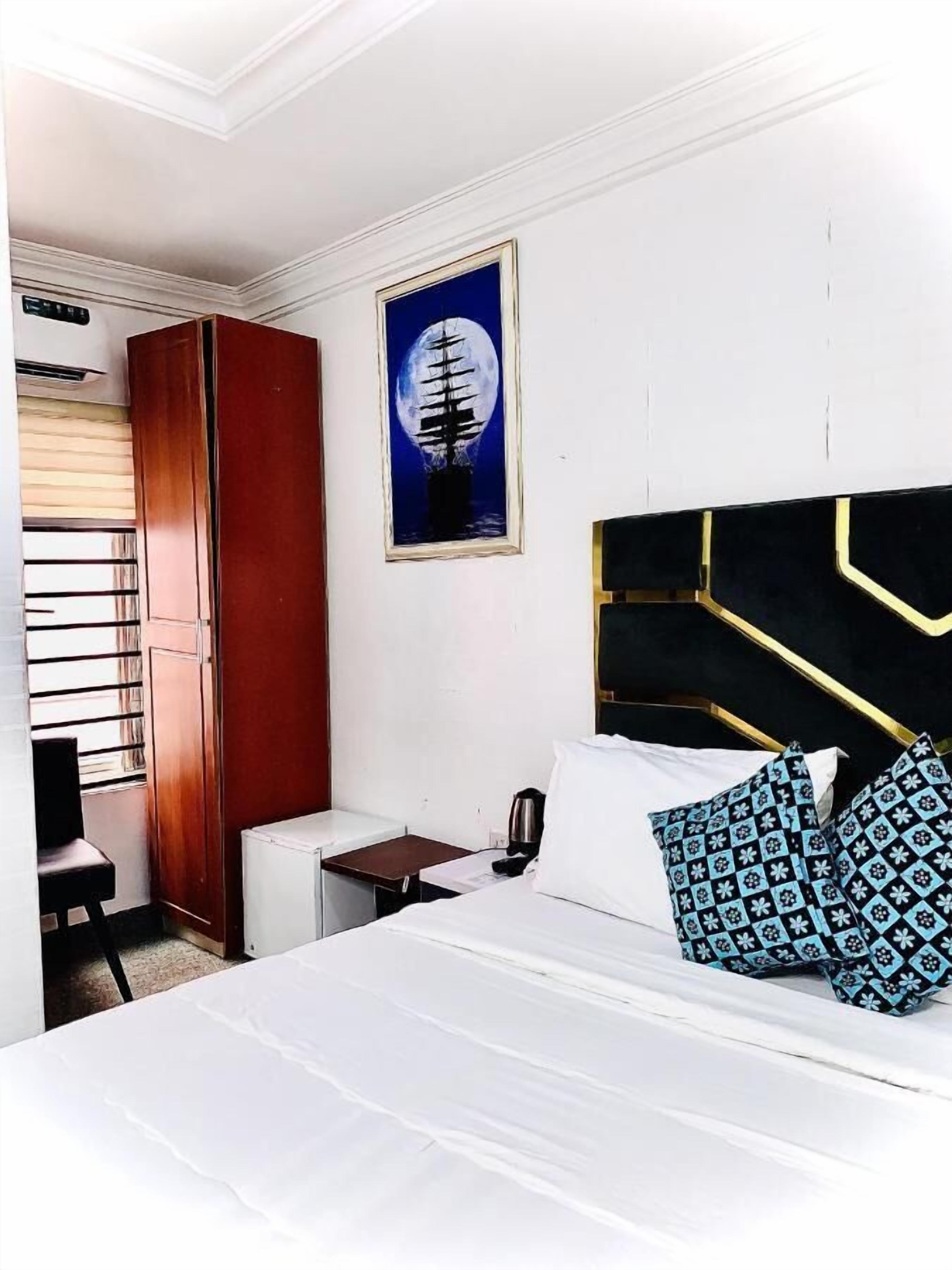 A hotel room with a bed, a desk, a wardrobe, and a painting of a ship on a moonlit sea.