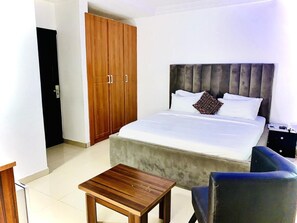 A bedroom with a bed, a wooden wardrobe, a small table, and a chair. - Vintage Suites and Apartment (Lagos)