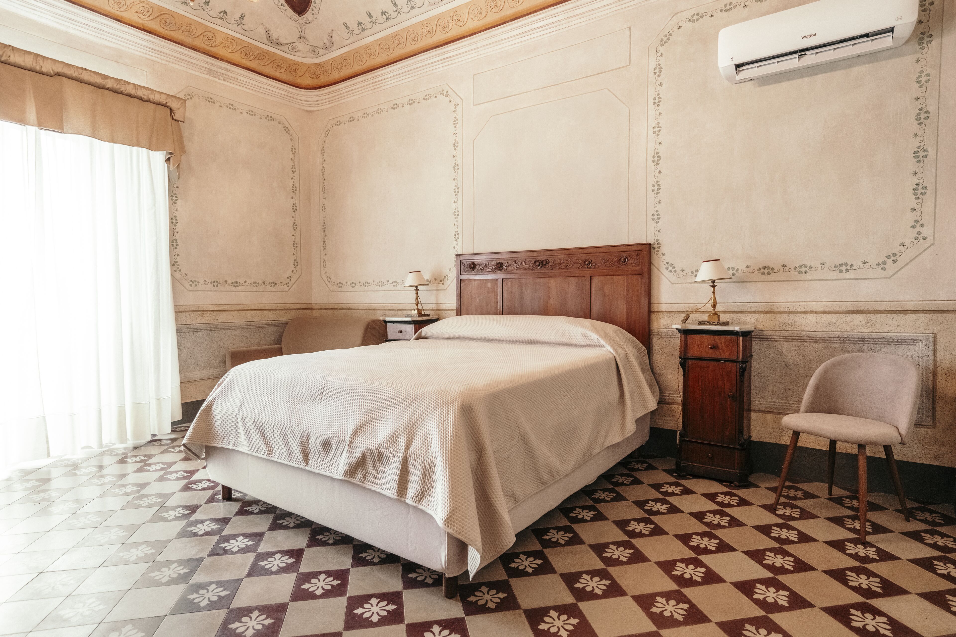 A bedroom with a checkered floor, a wooden bed, a nightstand, a chair, and an air conditioning unit.