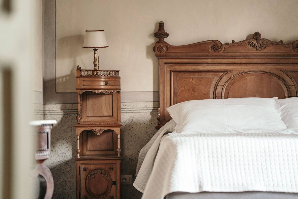Un lit en bois avec une tête de lit, une table de chevet avec une lampe et une étagère fixée au mur.