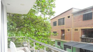 A balcony with white chairs, a metal railing, and a view of a brick building with multiple windows and a green awning. - Bello Amanecer a 1km de la Hacienda Nápoles (Antioquia)