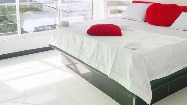 A modern hotel room with a large bed, white bedding, and a red accent pillow. - Bello Amanecer a 1km de la Hacienda Nápoles (Antioquia)