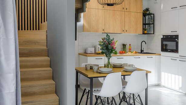 Une cuisine moderne avec un escalier en bois, des meubles blancs et un coin repas comprenant une table et des chaises.