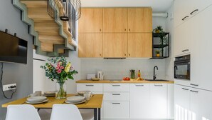Une cuisine moderne avec des meubles blancs, un escalier en bois et un coin repas avec des chaises blanches et un vase de fleurs.