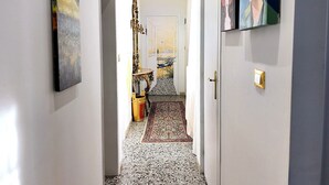 A hallway with a patterned carpet, artwork on the walls, and a door leading to a room with a bed and a nightstand. - 2 bedroom apartment in venice (Venezia)