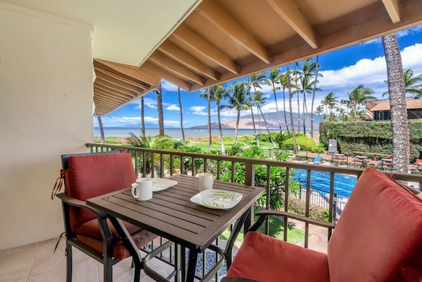Un balcon avec une table, des chaises et une vue sur l’océan et les palmiers.