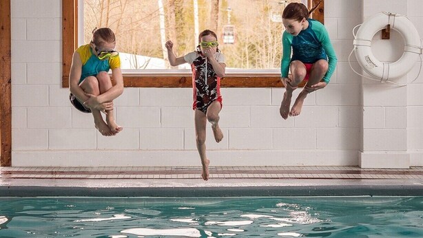 En swimmingpool med tre personer der hopper i.