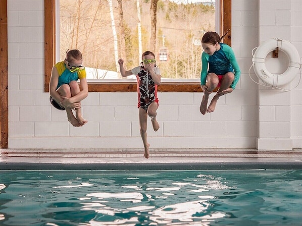 Una piscina con tres personas saltando al agua.