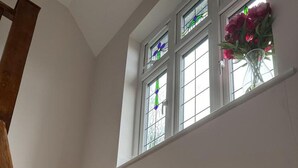 A staircase leading to a landing with three windows, each with stained glass and a vase of flowers. - Cosy and Lovely 4-bed House in Stanmore (Stanmore)