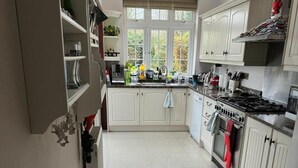A kitchen with white cabinets, a stove, and a sink. There is a window with a view of trees outside. - Cosy and Lovely 4-bed House in Stanmore (Stanmore)