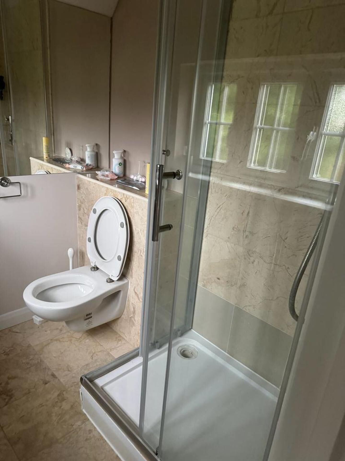 A bathroom with a glass-enclosed shower, a toilet, and a sink with toiletries.