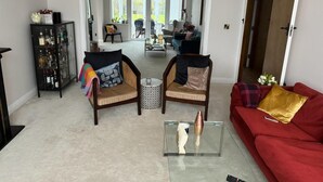 A living room with a red sofa, two armchairs, a glass coffee table, and a liquor cabinet. - Cosy and Lovely 4-bed House in Stanmore (Stanmore)
