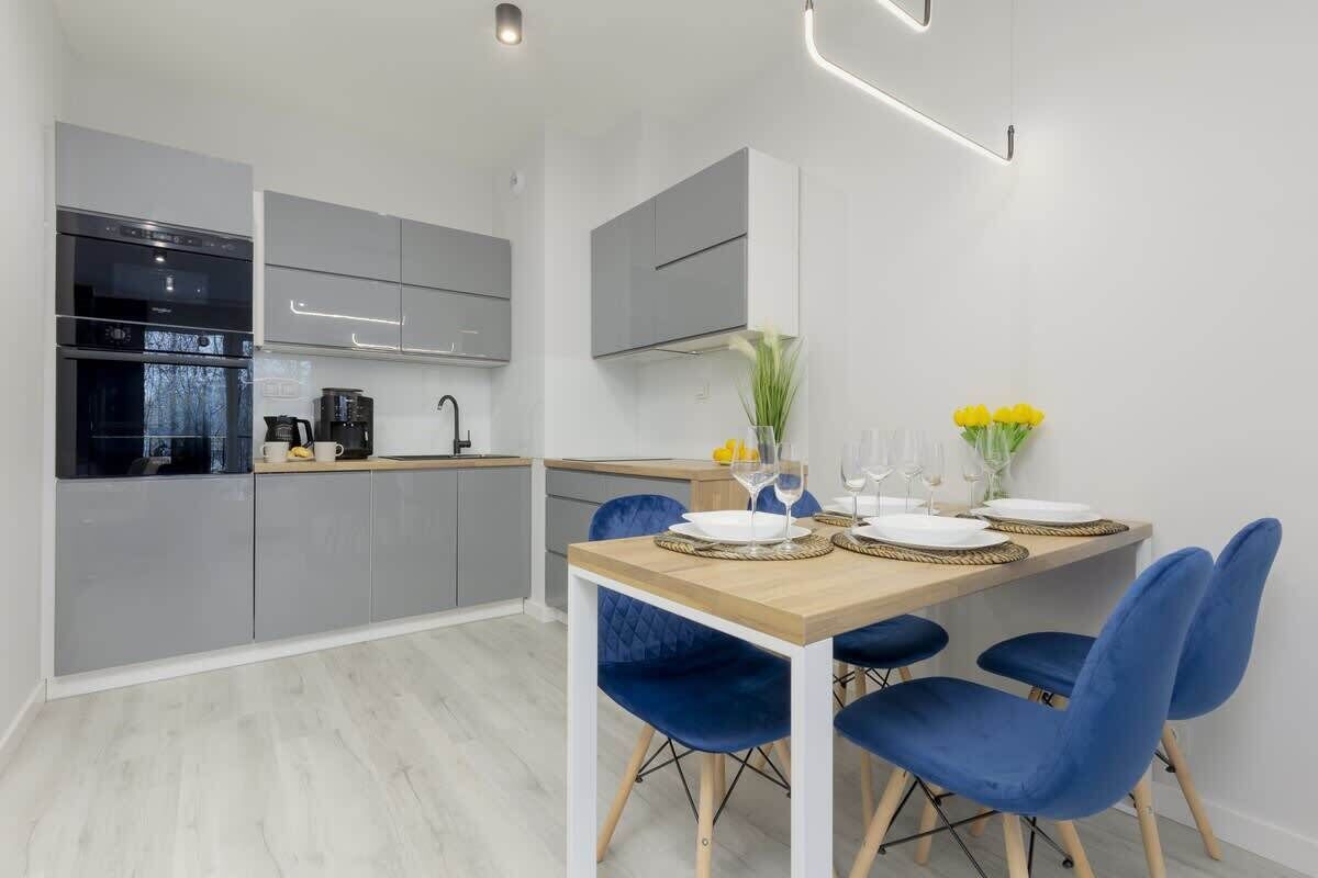 A modern kitchen with grey cabinets, a built-in oven, and a dining area with a wooden table and blue chairs.