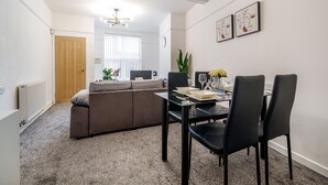 A modern living room with a sofa, a dining table with chairs, and a kitchen area in the background. - Next to Liverpool station stadium city (Liverpool)